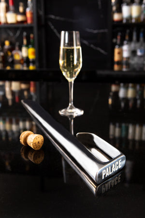 Champagne sabre laying on marble bar with flute in the background